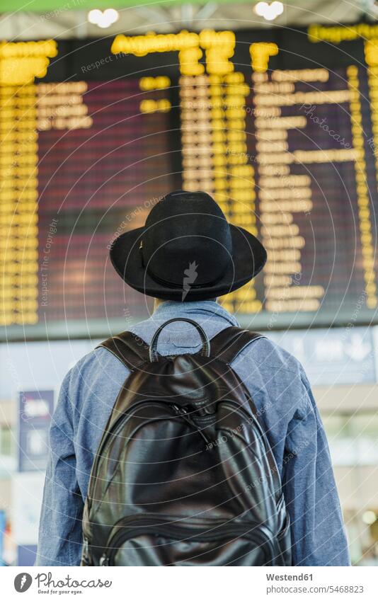 Young man with hat and backpack looking at arrival departure board at the airport hats view seeing viewing men males Arrival Departure Board rucksacks backpacks