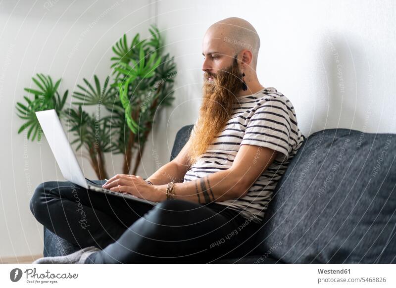 Hipster sitting on couch at home using laptop mobile working individuality Distinct looking down casual leisure wear casual clothing casual wear casual clothes