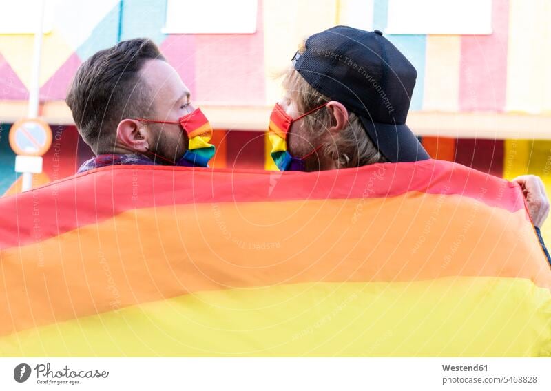 Gay boyfriends wearing masks holding rainbow flag color image colour image Spain leisure activity leisure activities free time leisure time outdoors