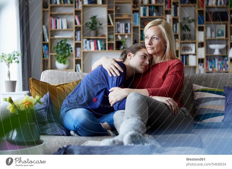 Mother and adolescent daughter sitting on couch with arms around caucasian caucasian ethnicity caucasian appearance european Hygge Security Secure cozy sociable