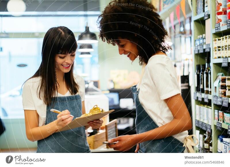 Two smiling women in a store with clipboard smile shop clipboards clip-board clip-boards clip board woman females retail trade trading Adults grown-ups grownups