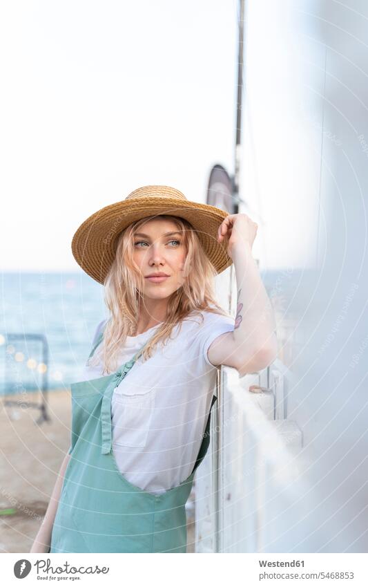 Young woman spending a day at the seaside, wearing straw hat relax relaxing stand free time leisure time stylish Lifestyle beaches location shot location shots