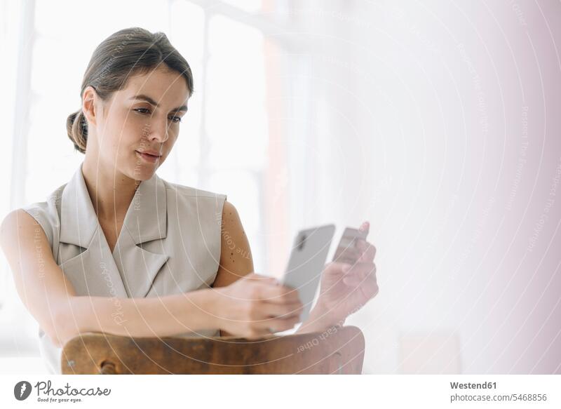 Businesswoman holding credit card while using mobile phone at office color image colour image indoors indoor shot indoor shots interior interior view Interiors