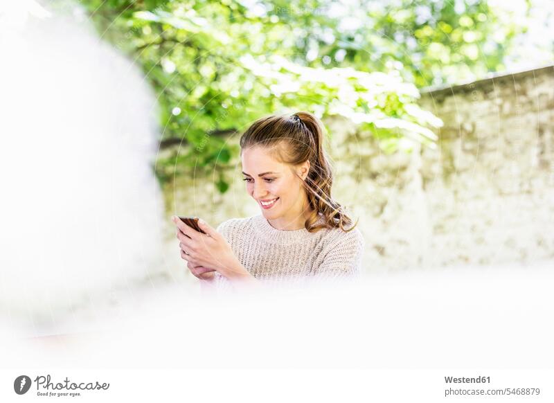 Smiling woman looking at cell phone outdoors Smartphone iPhone Smartphones eyeing females women smiling smile mobile phone mobiles mobile phones Cellphone