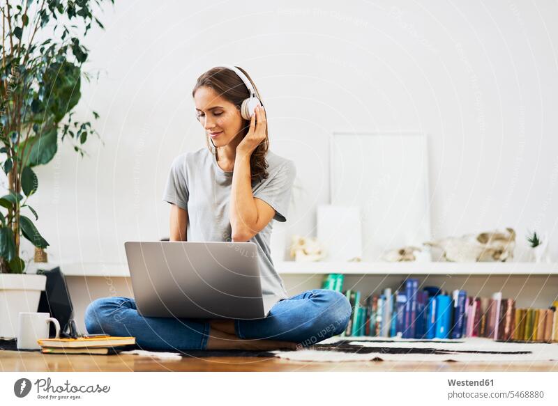 Relaxed young woman at home sitting on the floor using laptop and listening to music relaxed relaxation Seated Laptop Computers laptops notebook floors females