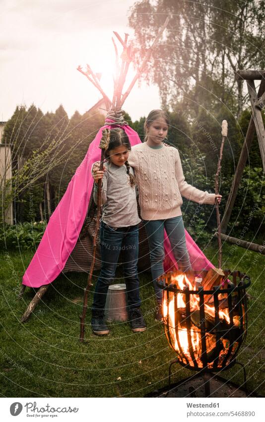 Two girls wearing feather headdress, with twist bread, looking into fire Camp Fire Campfire Bonfire garden gardens domestic garden tent tents females view