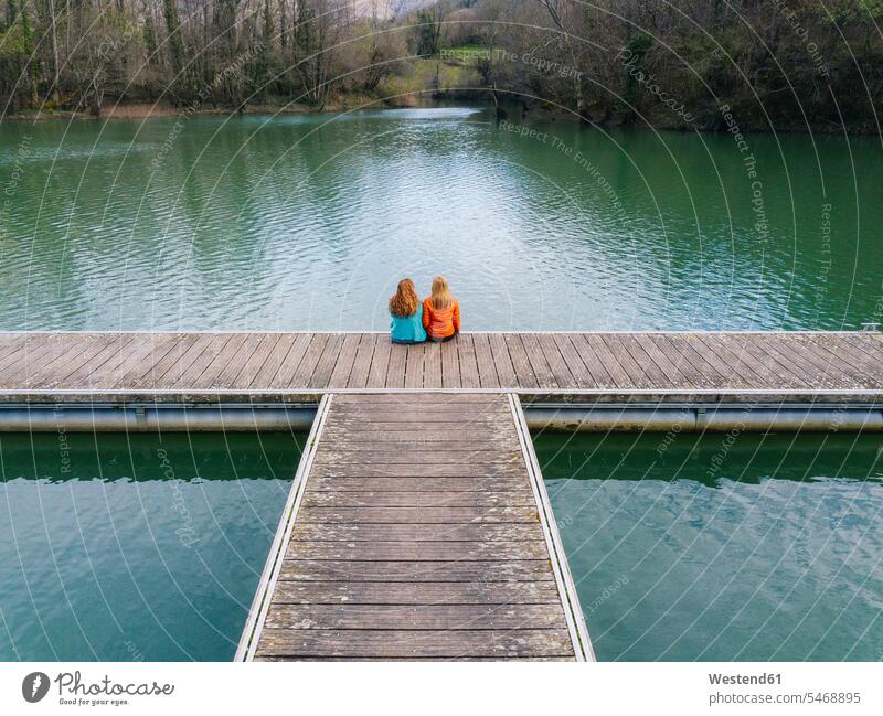 Back view of two friends sitting side by side on jetty, Valdemurio Reservoir, Asturias, Spain relax relaxing Seated enjoy enjoyment indulgence indulging