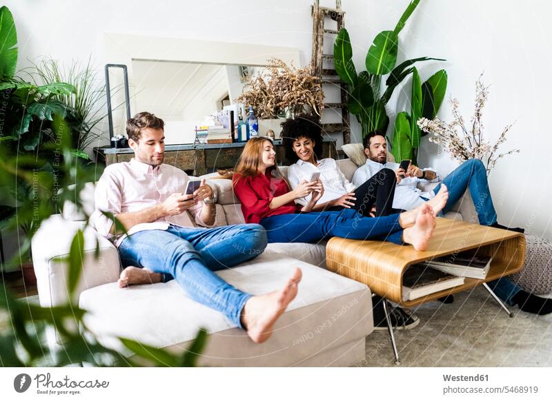 Friends sitting on couch, working casually together, using smartphones friends use settee sofa sofas couches settees Smartphone iPhone Smartphones At Work