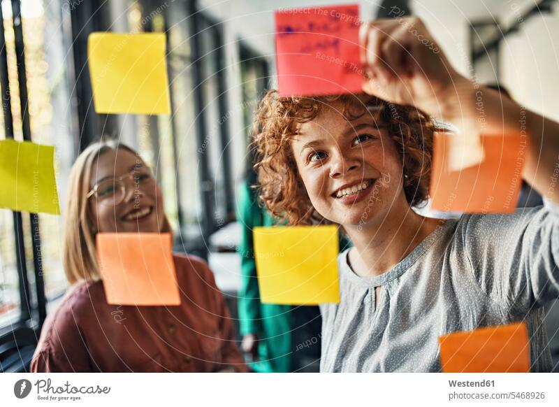 Happy colleagues with sticky notes at glass pane in office Occupation Work job jobs profession professional occupation business life business world