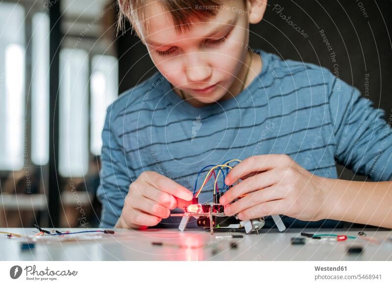 Boy assembling robot at home animals creature creatures cables power cord Tables toys robots discover discovering shine play delight enjoyment Pleasant pleasure