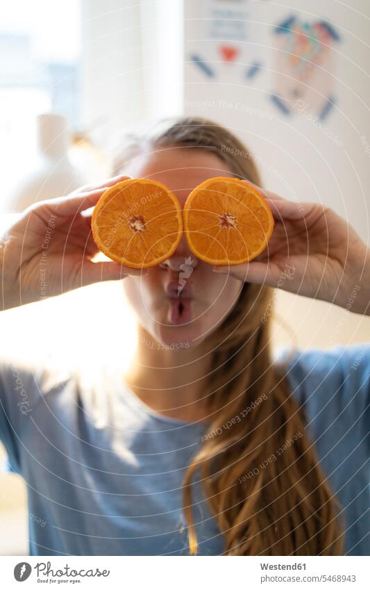 Playful young woman covering her eyes with oranges at home human human being human beings humans person persons celibate celibates singles solitary people