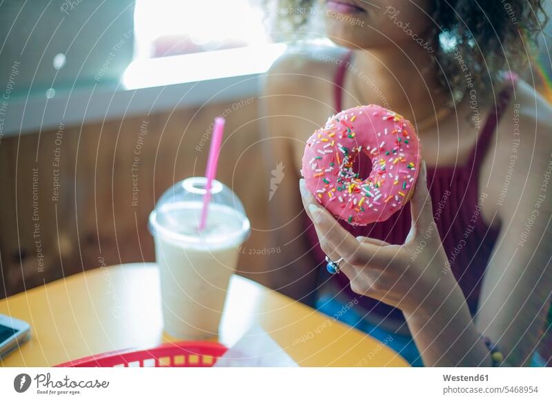 Young woman eating doughnut while sitting at cafe color image colour image day daylight shot daylight shots day shots daytime Seated casual clothing casual wear