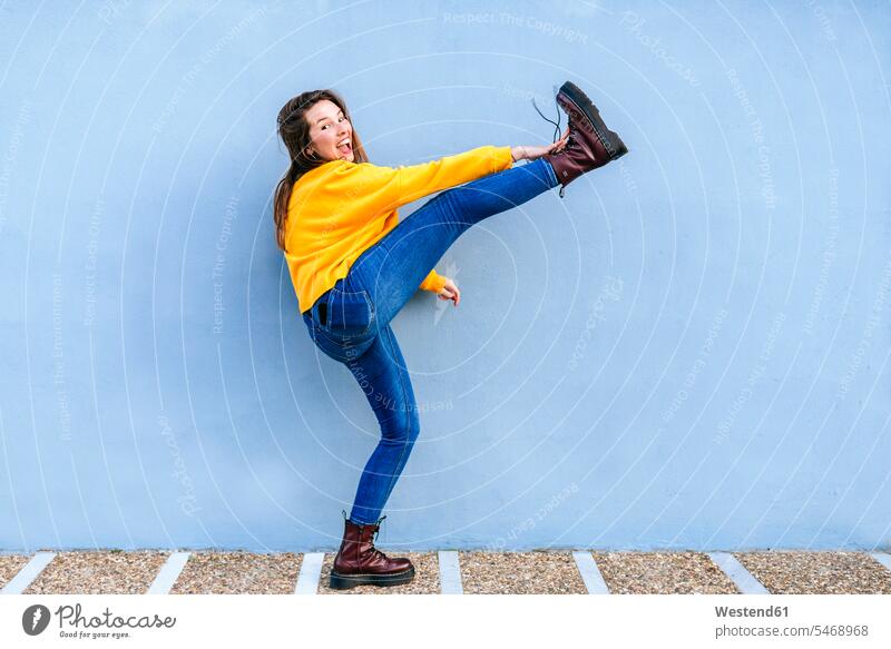 Playful young woman with raised leg at blue wall legs human leg human legs walls playful females women people persons human being humans human beings Adults