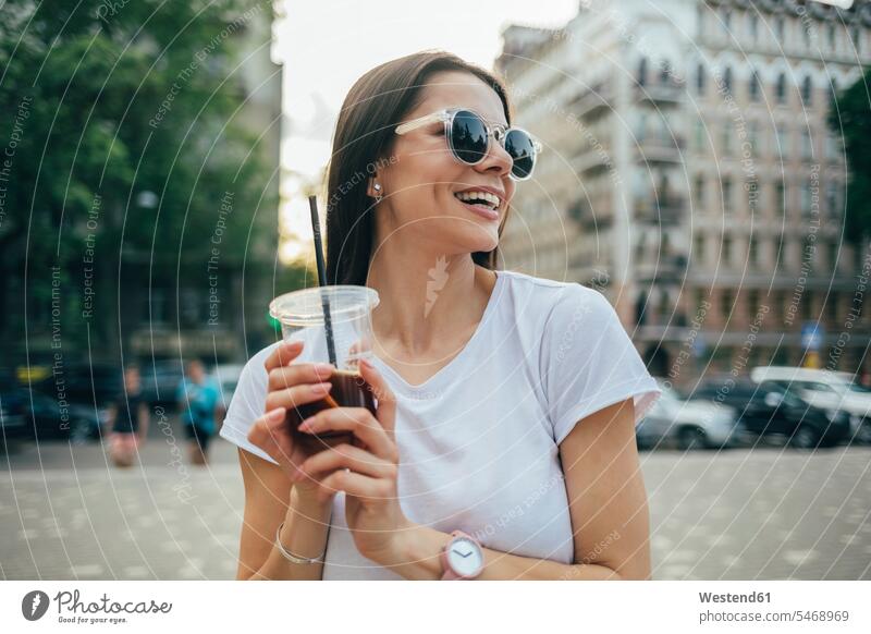 Cheerful beautiful woman wearing sunglasses holding soft drink while standing in city color image colour image Ukraine leisure activity leisure activities