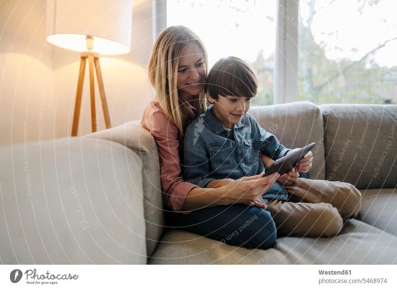 Mother and son sitting on couch, using digital tablet windows couches settee settees sofa sofas Seated Secure at home comfortable cosy sociable Technological