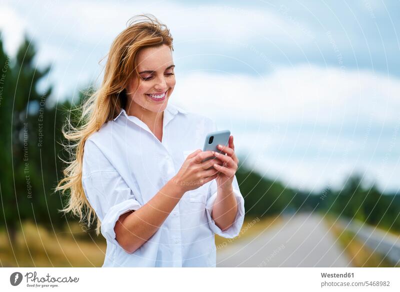 Happy woman checking cell phone on rural road touristic tourists telecommunication phones telephone telephones cell phones Cellphone mobile mobile phones
