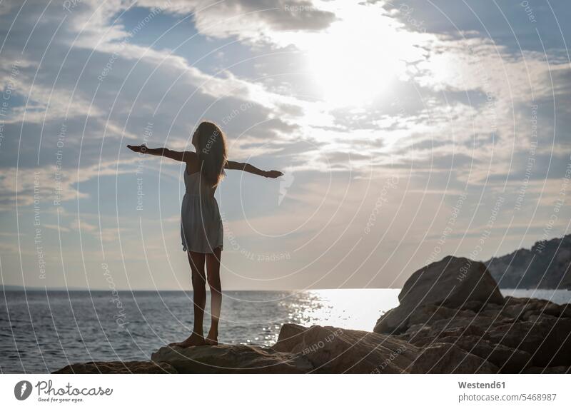 Croatia, Lokva Rogoznica, back view of girl with arms outstretched standing on a rock at dusk atmosphere atmospheric evening evening twilight rocks females