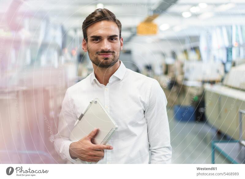 Confident young male engineer holding digital tablet while standing at illuminated factory color image colour image indoors indoor shot indoor shots interior
