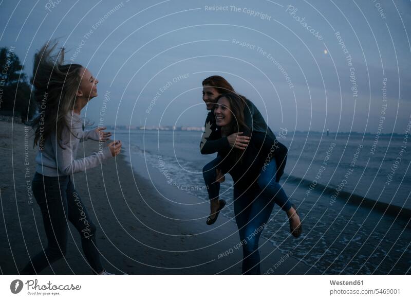 Germany, Hamburg, carefree mother with two teenage girls on the beach at Elbe shore at night by night nite night photography happiness happy water's edge