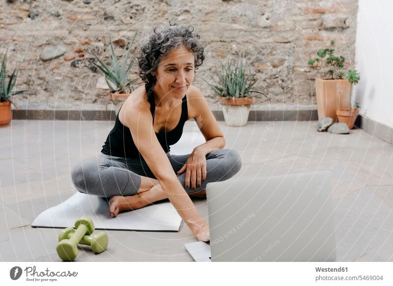 Smiling woman using laptop for learning yoga through online tutorial while sitting at back yard color image colour image Spain outdoors location shots