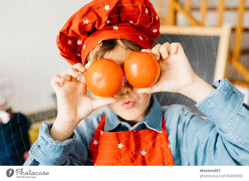 Playful boy covering his eyes with tomatoes in kitchen Chefs cook cooks hold delight enjoyment Pleasant pleasure Cheerfulness exhilaration gaiety gay glad