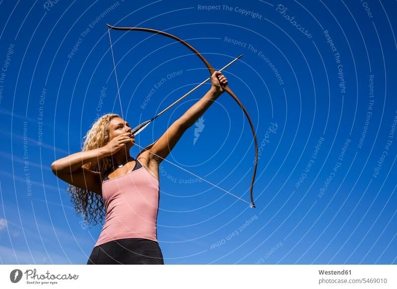 Archeress aiming with bow against blue sky skies archers female archer archeress Archery Bows bows bowmen bowman archery shooting sports hobby hobbies