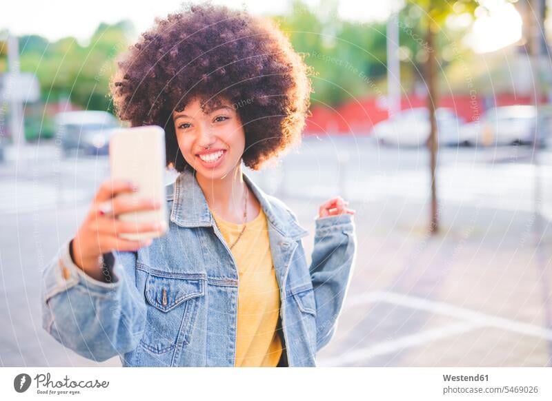 Happy young woman with afro hairdo taking a selfie in the city human human being human beings humans person persons curl curled curls curly hair jewelry