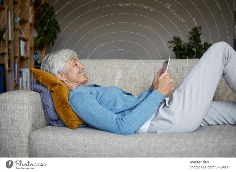 Smiling woman using digital tablet while lying down on sofa at home color image colour image indoors indoor shot indoor shots interior interior view Interiors