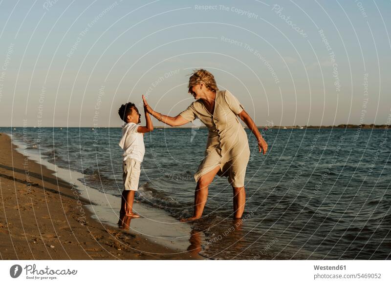 Happy grandmother and grandson doing high five to each other at beach during sunset color image colour image outdoors location shots outdoor shot outdoor shots