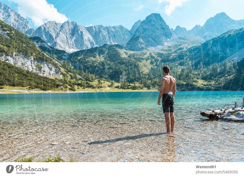 Austria, Tyrol, Young man at Lake Seebensee standing ankle deep in water mountain lake mountain lakes tranquility tranquillity Calmness journey travelling