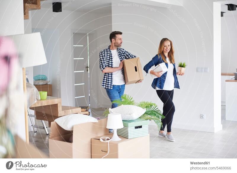Couple moving into new flat carrying cardboard box and plant cardboard boxes packing case packing cases move in couple twosomes partnership couples Plant Plants
