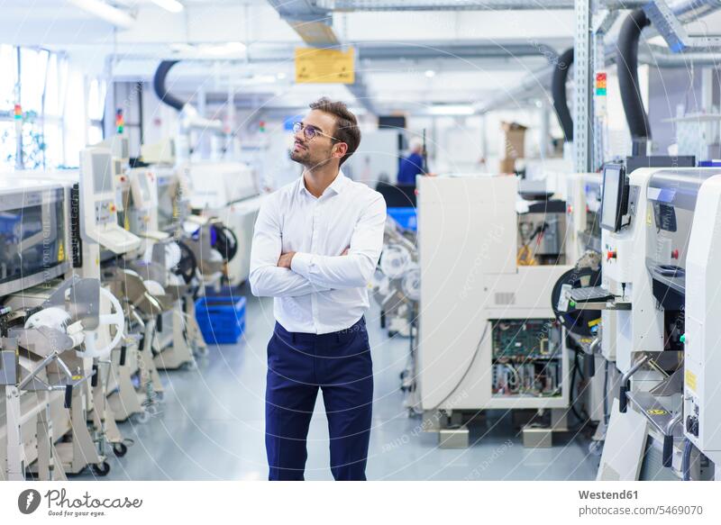 Thoughtful young businessman standing with arms crossed while looking away at illuminated factory color image colour image indoors indoor shot indoor shots
