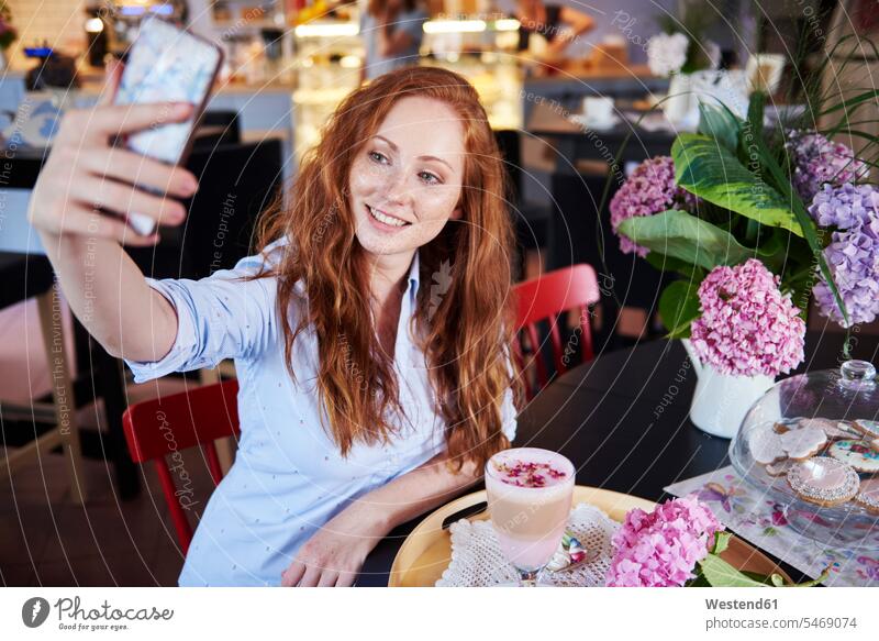 Smiling young woman taking a selfie in a cafe mobile phone mobiles mobile phones Cellphone cell phone cell phones Selfie Selfies Drink beverages Drinks Beverage