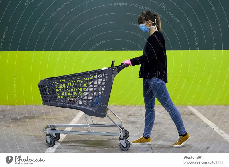 Woman wearing mask walking with shopping cart against wall color image colour image outdoors location shots outdoor shot outdoor shots day daylight shot