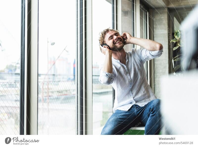 Happy casual young man listening to music with headphones at the window happiness happy hearing headset men males windows Adults grown-ups grownups adult people