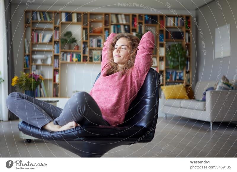 Mid adult woman with hands behind head relaxing on chair at home color image colour image indoors indoor shot indoor shots interior interior view Interiors day