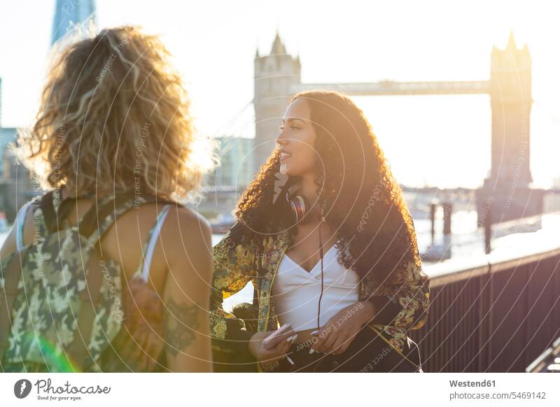 UK, London, two friends together in the city with Tower Bridge in background at sunset female friends bridge bridges town cities towns sunsets sundown woman