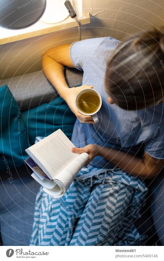 Top view of young woman reading book on couch at home human human being human beings humans person persons celibate celibates singles solitary people