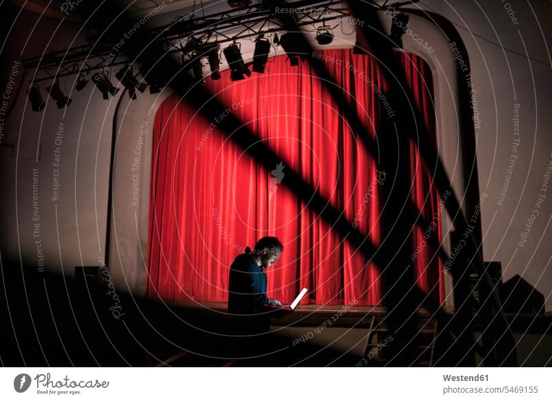 Director standing in front of stage at theatre using laptop theater theaters theatres Stage Theater man men males auditorium director stage director use