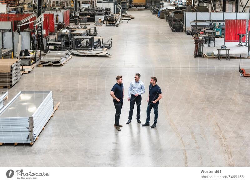 Three men standing and talking on factory shop floor colleagues production hall factories man males speaking Adults grown-ups grownups adult people persons