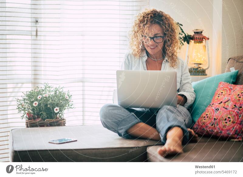 Smiling woman using laptop on couch at home dyed hair cozy sociable comfortable cosy working from home working at home Work From Home females women