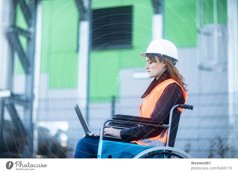 Young technician with safety helmet and vest in wheelchair working on laptop outdoors woman females women Laptop Computers laptops notebook wheelchairs At Work