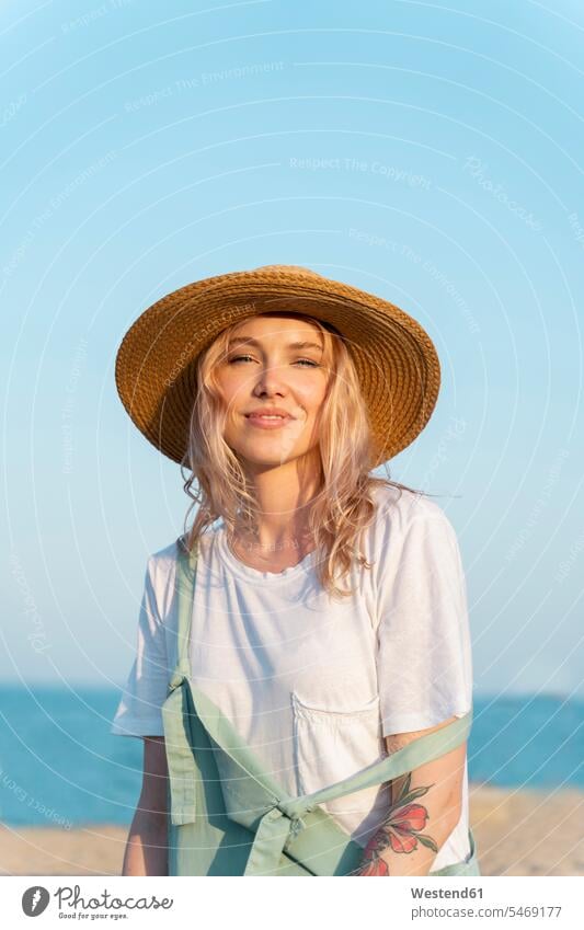 Young woman spending a day at the seaside, wearing straw hat, portrait smile happy Contented Emotion pleased stand free time leisure time Distinct individual