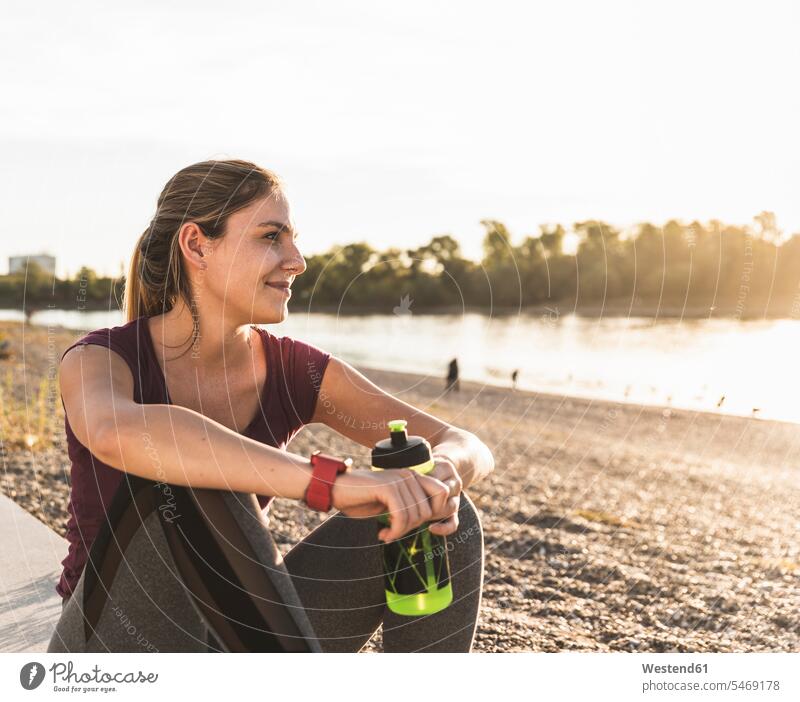 Young woman taking a break after exercising at the river River Rivers recovering Refreshment refreshing sitting Seated exercise training practising young women