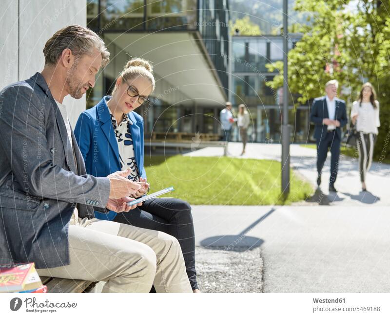 Colleagues with tablet sitting on bench outside office building office buildings business people businesspeople digitizer Tablet Computer Tablet PC