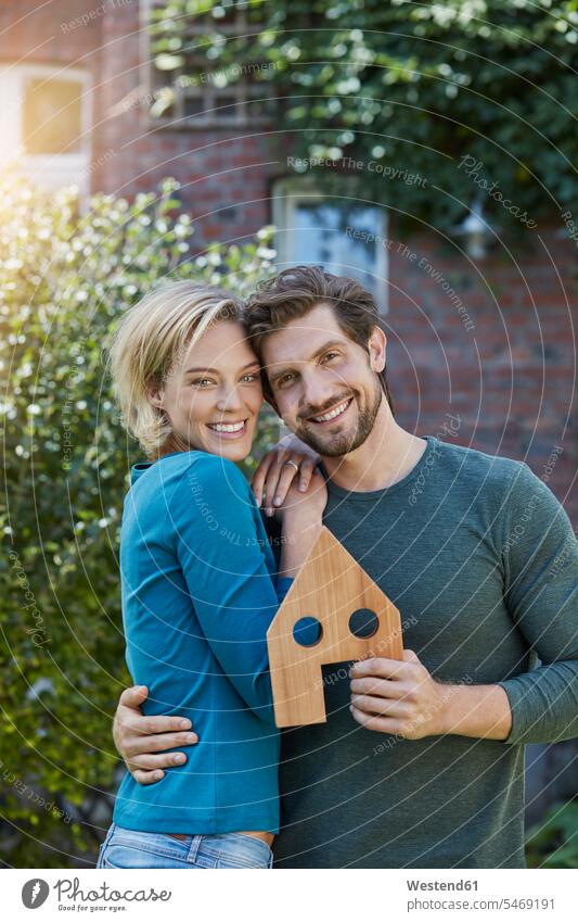 Portrait of happy couple in front of their home with house model twosomes partnership couples happiness houses models portrait portraits people persons