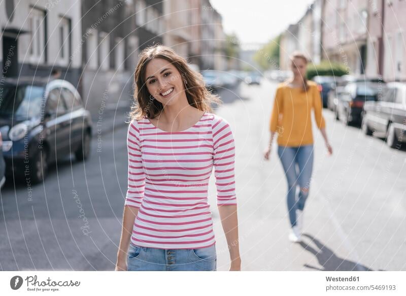 Woman walking in street, followed by friend female friends city town cities towns going following mate friendship outdoors outdoor shots location shot