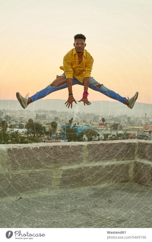 Young man in a yellow shirt jumping from a wall at sunset shirts jumps Leaping in the evening Ardor Ardour enthusiasm enthusiastic excited free time