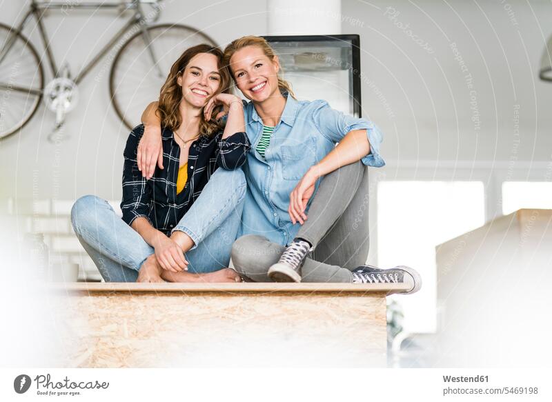 Two young women sitting cross-legged on the counter of their coffee shop,with arms aroug human human being human beings humans person persons