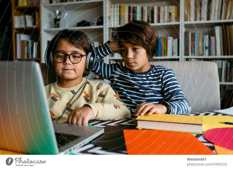 Boy looking at laptop with hand in hair while homeschooling with male friend in living room color image colour image 8-9 years 8 to 9 years children kid kids